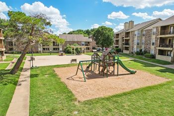 A playground with a green slide and a brown sandbox in the middle of a grassy area